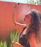 Woman with curly hair using ZAYNA Fresh Blossom Face Mist outdoors in sunlight for a refreshing skincare routine